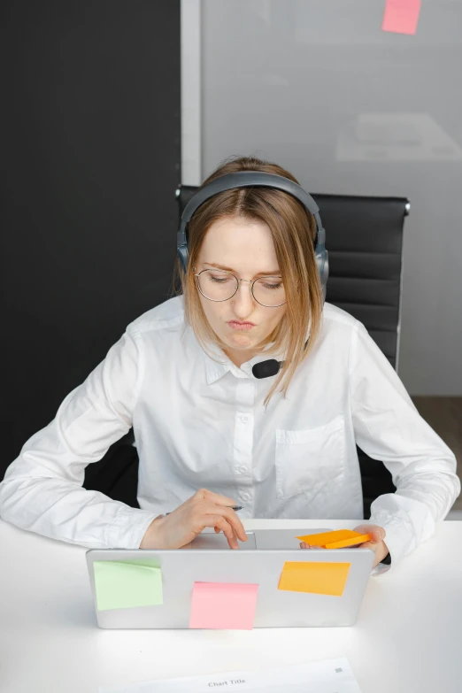 a woman sitting at a table in front of a laptop, wearing a headset, looking distracted and awkward, teaching, modified