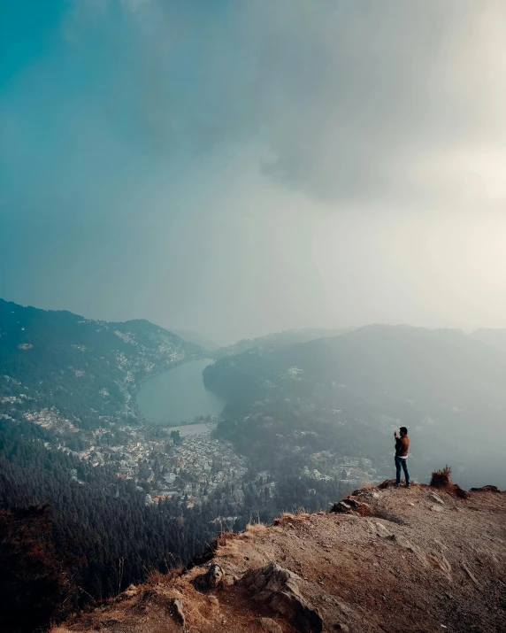 a couple is standing on a rocky outcropping with view of the town below