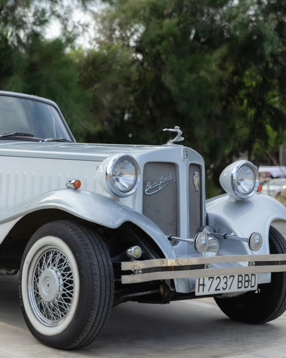 a silver car is parked in a parking lot, art deco influence, silver，ivory, convertible, no cropping