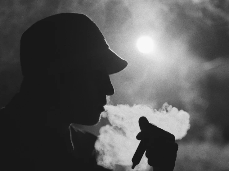 a black and white photo of a man smoking a cigarette, by John Hutton, unsplash, silhouette, holding a small vape, sun behind him, steam clouds