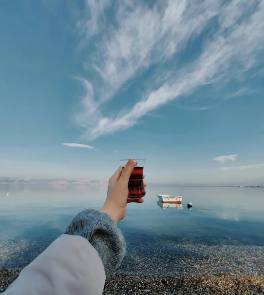 a person taking a picture of a body of water, by Niko Henrichon, pexels contest winner, surrealism, beer in hand, clear skies, azure and red tones, cold brew coffee )