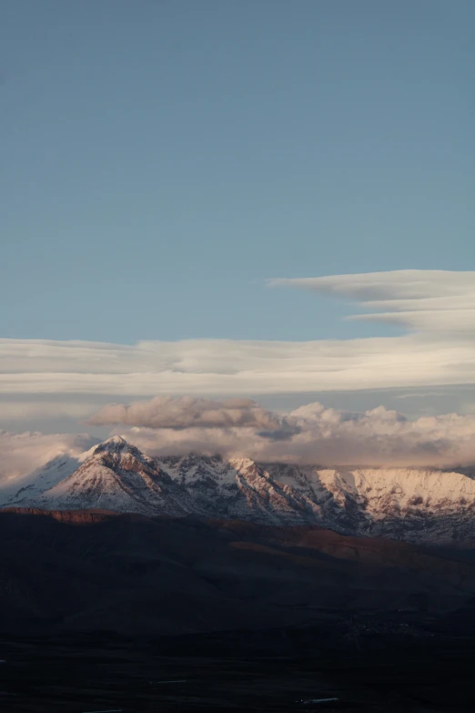 clouds float over a snowy mountain range under blue skies