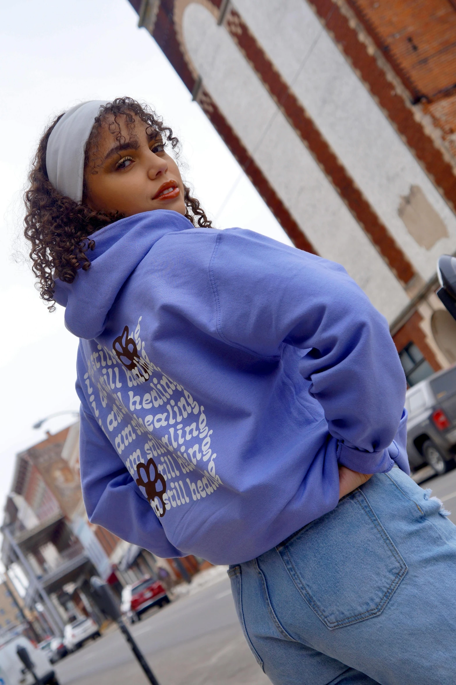 a woman standing next to a parking meter, an album cover, instagram, graffiti, blue hoodie, lilac, profile image, patterned clothing