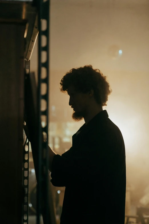 a man standing on top of a roof next to a tall building, an album cover, by Thomas Wijck, pexels contest winner, curly haired, standing in a server room, cinematic back lit lighting, profile portrait