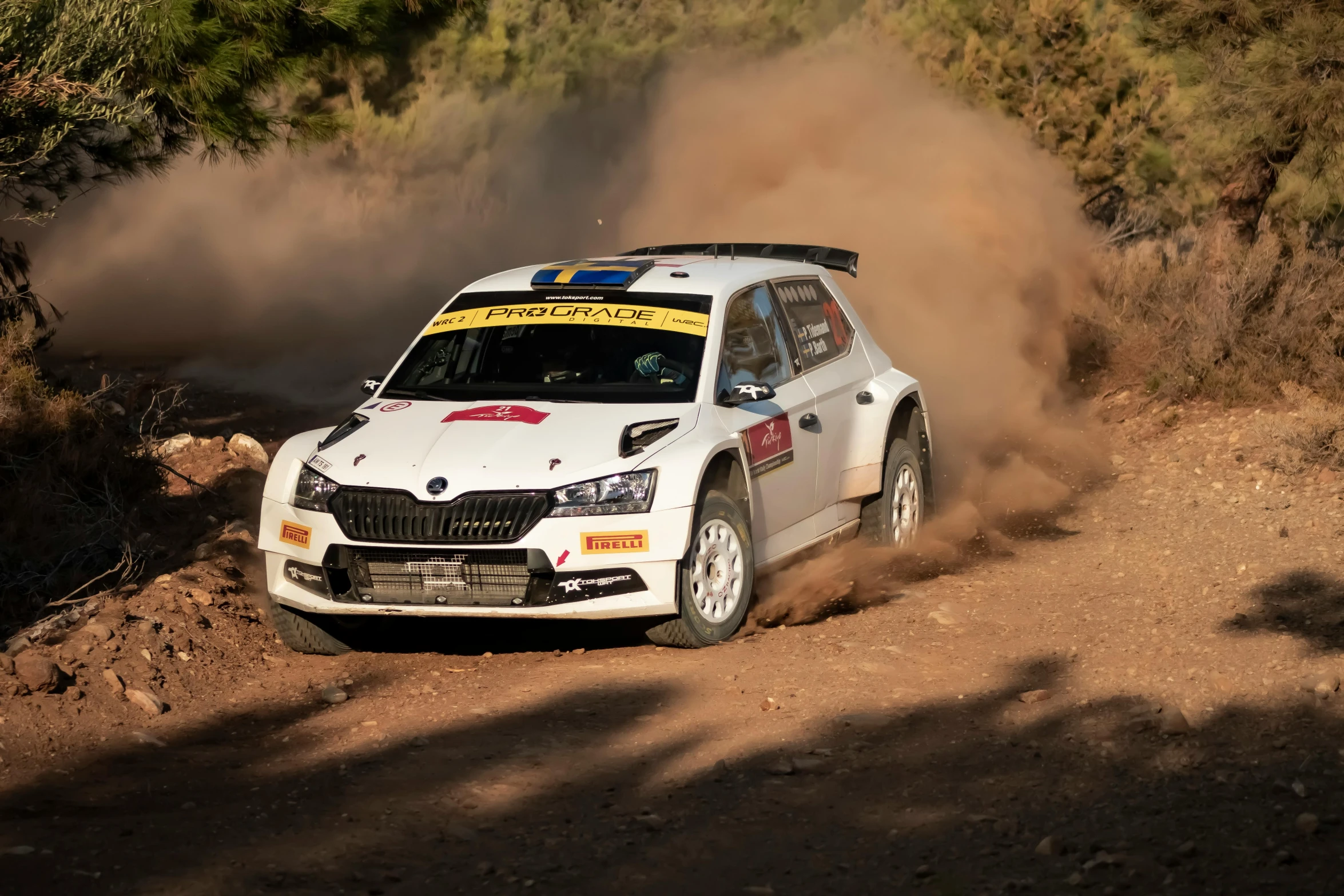 a white rally car with a yellow number on it is driving through the dirt