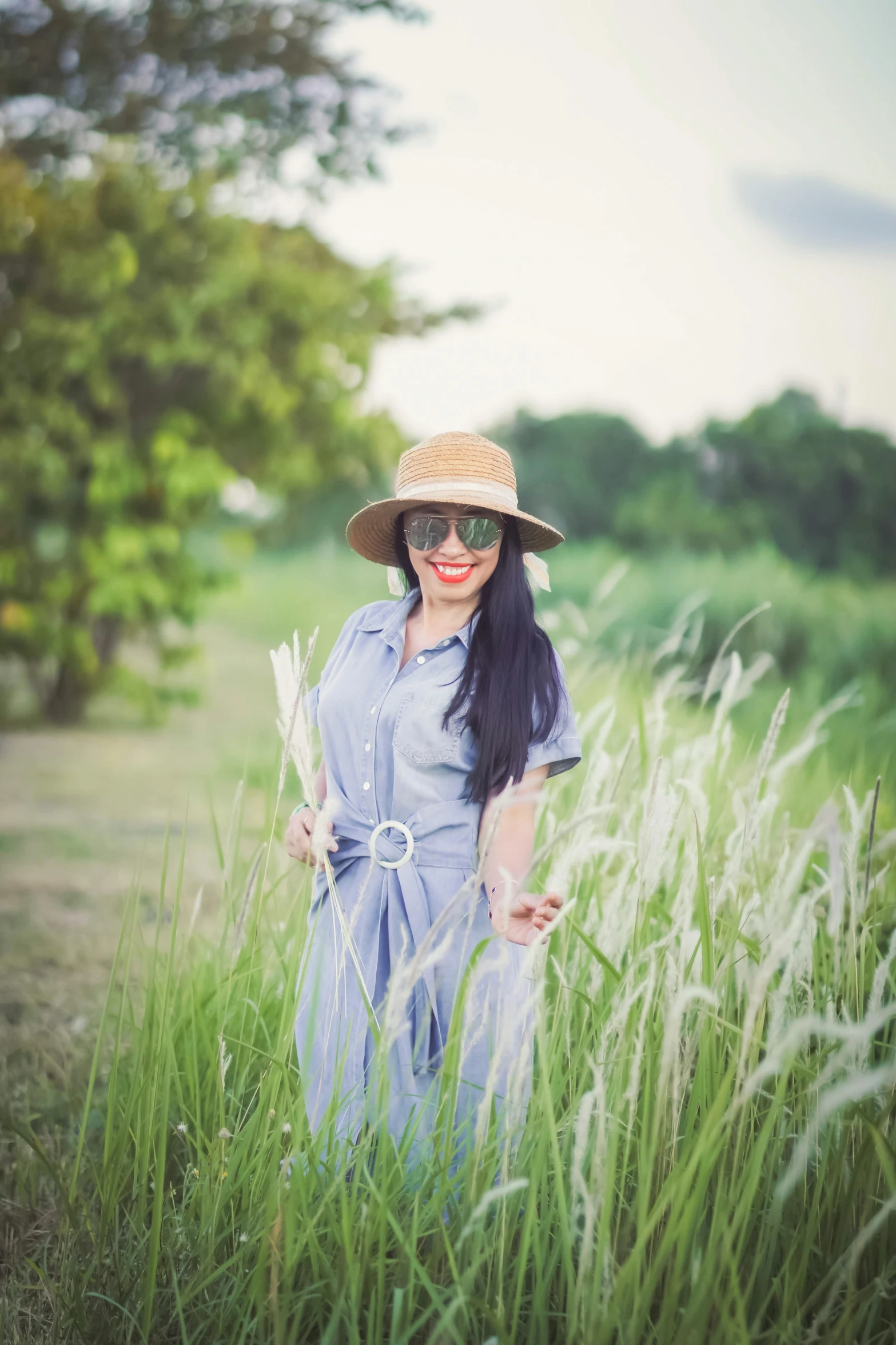 a woman wearing sunglasses and hat walking through tall grass