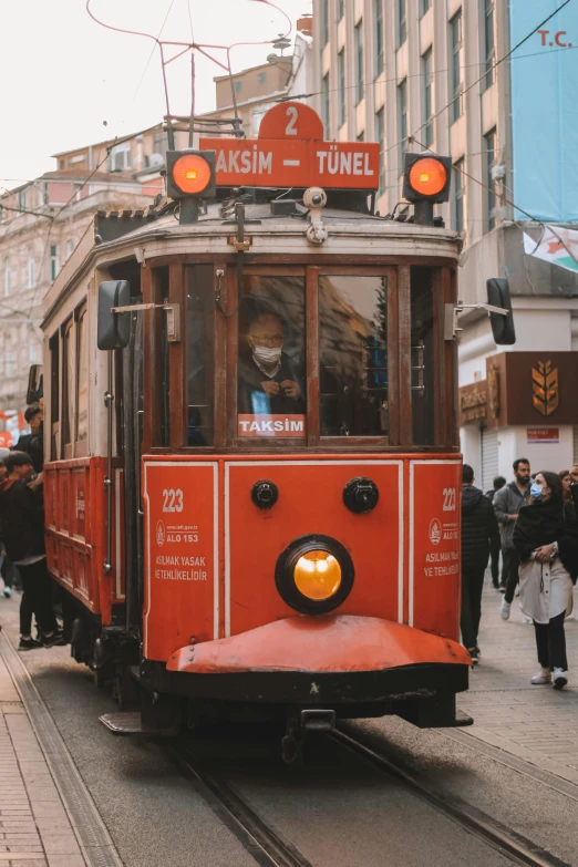 a red trolley traveling down a street next to tall buildings, by irakli nadar, pexels contest winner, art nouveau, ottoman sultan, brown, gif, bustling with people