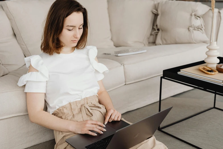 a woman sitting on a couch using a laptop, a portrait, trending on pexels, girl with brown hair, white sleeves, low quality photo, office clothes