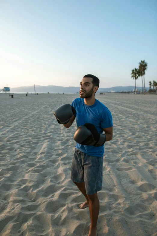 a man is standing in the sand holding some boxing gloves