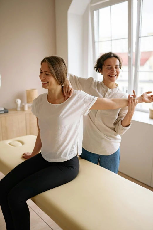 a couple of women sitting on top of a table, stretching to walls, recovering from pain, broad shoulder, highly technical
