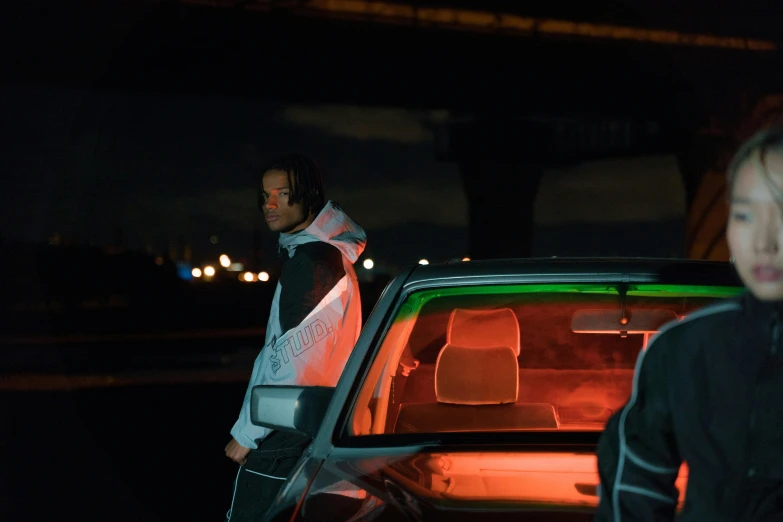 two people stand next to a car at night