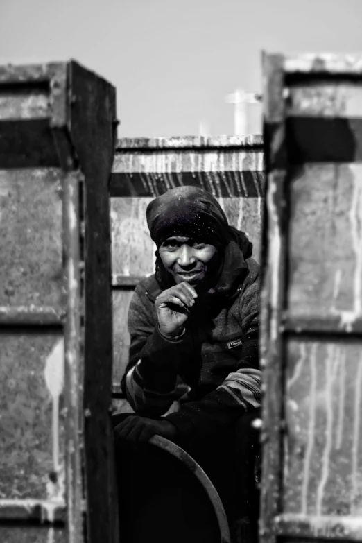 a black and white photo of a man sitting in a doorway, by Kevin Connor, unsplash, shanty town, freezing, happy face, stood in a cell