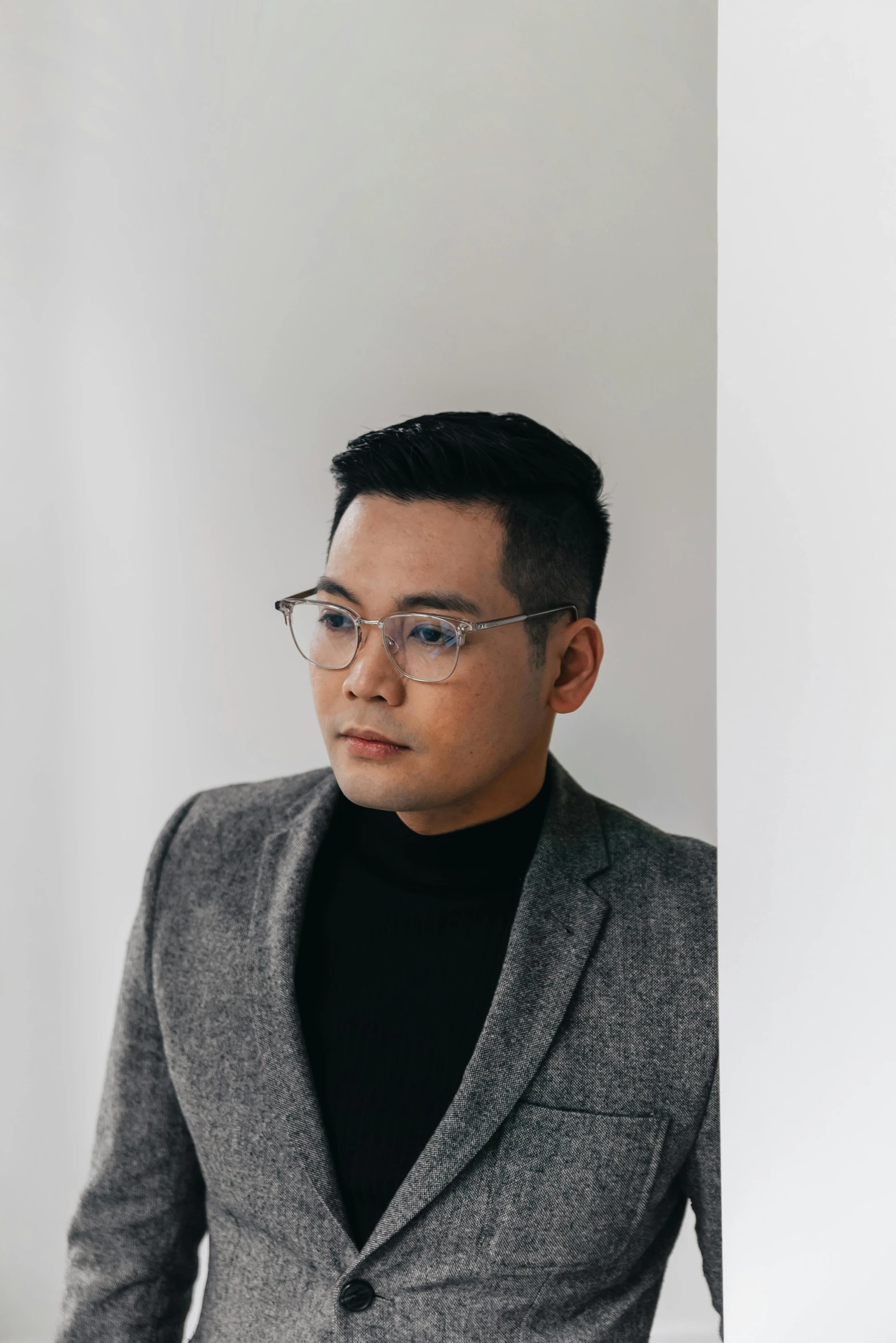 a man in a suit leaning against a wall, bao pham, wearing a turtleneck and jacket, wearing black frame glasses, man in his 30s