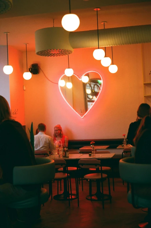 a group of people sitting at a table in a restaurant, by Jacob Toorenvliet, pexels, romanticism, neon heart reactor, pastel pink neon, helsinki, warm lighting inside