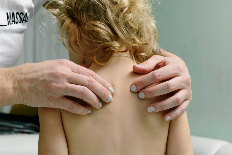 a woman getting her back examined by a doctor, by David Simpson, unsplash, young child, manuka, showing her shoulder from back, soft emotion