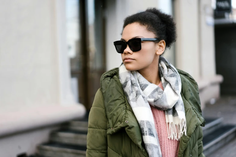 a woman wearing a green jacket and scarf, trending on unsplash, square glasses, mixed race woman, wearing oakley sunglasses, tuffle coat