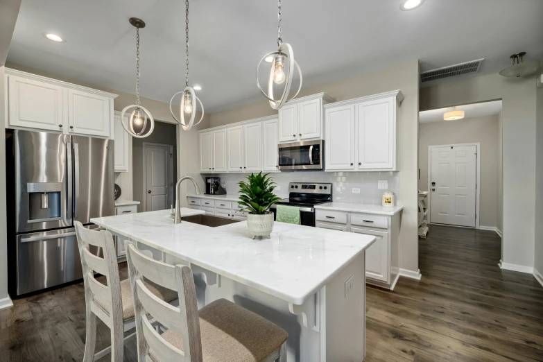 a white kitchen with large island countertop and a metallic fridge