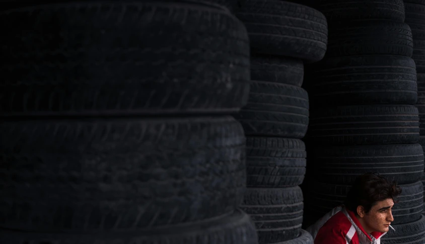 a man sitting in front of a stack of tires, unsplash, renaissance, background image, black and red, product shot, small details