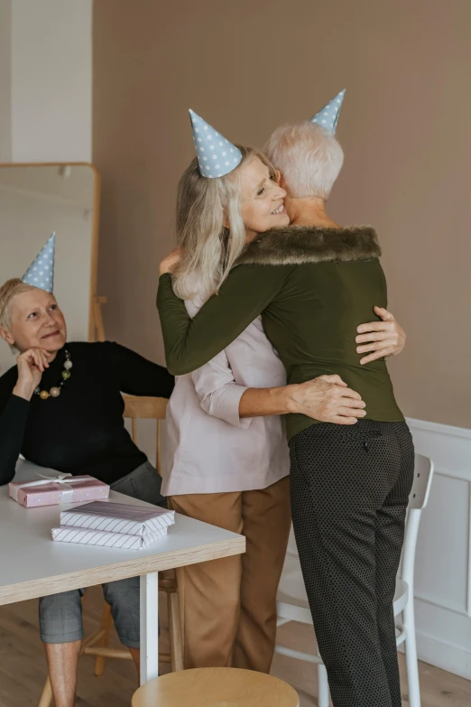 a couple of people that are hugging each other, a colorized photo, pexels contest winner, party hats, older woman, gifts, delightful surroundings