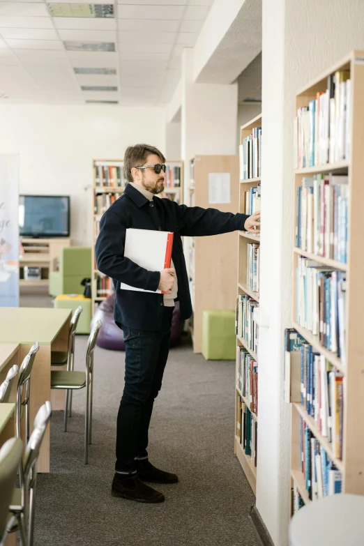 a man standing in front of a bookshelf in a library, reddit, academic clothing, russian academic, overlooking, teaching