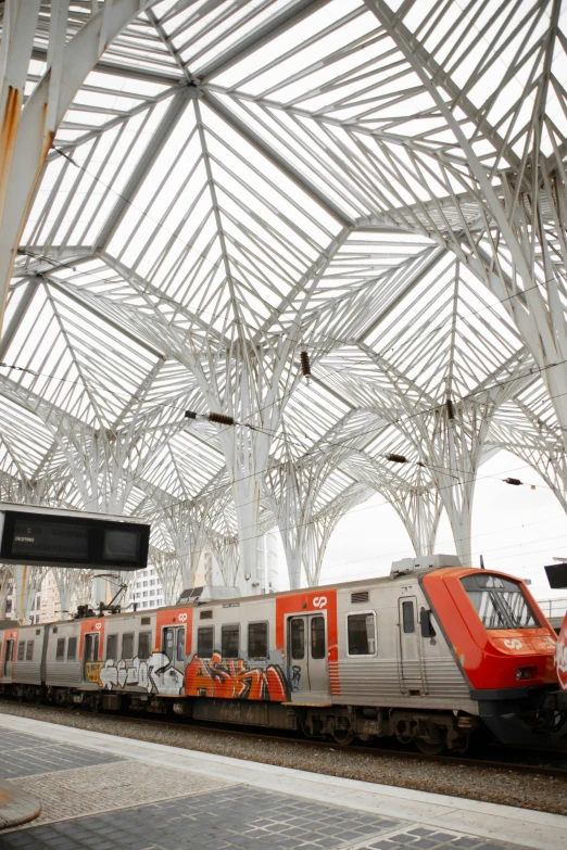 a red train parked in the terminal surrounded by covered structures