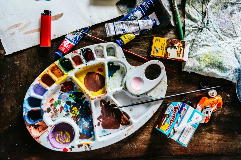 a paint palette sitting on top of a wooden table, by Julia Pishtar, trending on pexels, process art, inside a cluttered art studio, flatlay, jonathan yeo painting, paint tubes
