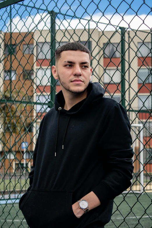 a man standing on top of a tennis court holding a racquet, an album cover, inspired by Carlos Berlanga, unsplash, graffiti, in a black hoodie, headshot profile picture, slightly smiling, standing in a city street