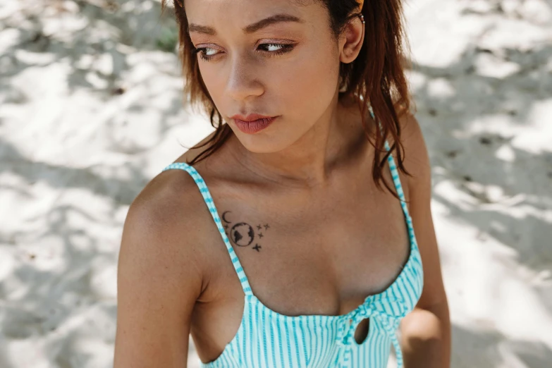 a beautiful young woman standing on top of a sandy beach, a tattoo, inspired by Valéria Dénes, trending on pexels, left eye stripe, wearing a camisole, turqouise, close-up from above