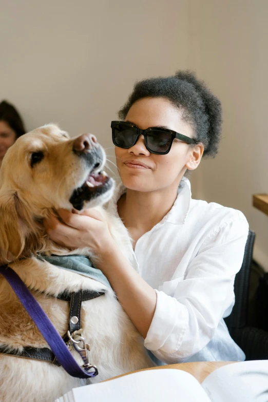 a woman sitting at a table with a dog, a portrait, trending on unsplash, implanted sunglasses, tessa thompson, in a lab, blind