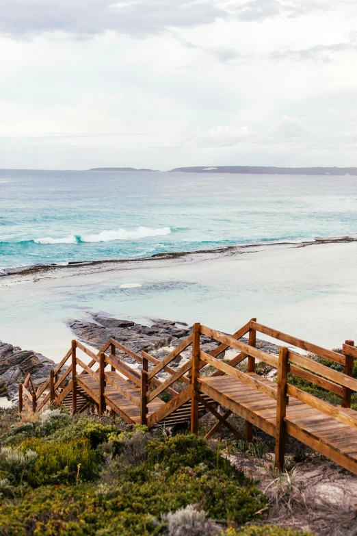 a wooden walkway leading to a beach next to the ocean, rock pools, outdoor staircase, high vantage point, the emerald coast