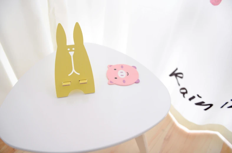 a table with a cutout of a rabbit and a pig on it, a cartoon, inspired by Peter Alexander Hay, unsplash, private press, koda kazuma, yellow, product view, small room