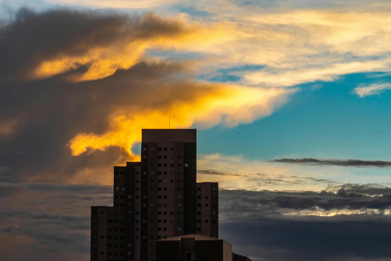 a couple of tall buildings sitting next to each other, by Sven Erixson, pexels contest winner, brutalism, sunset clouds, new mexico, golden clouds, the photo was taken from afar