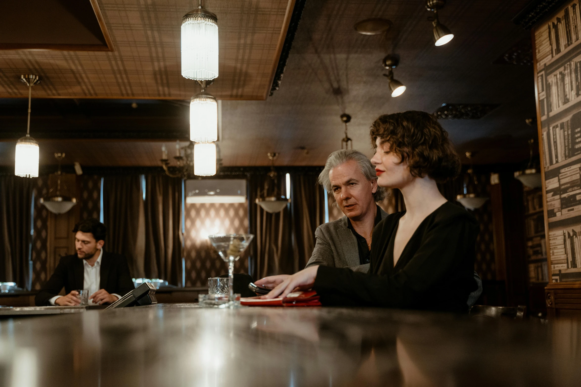 two people sit at a bar and one woman looks down