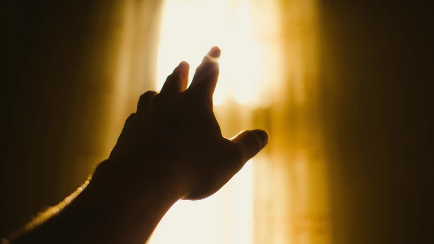 a person holding their hand up in front of a window, pexels, light and space, warm golden backlit, prayer, instagram post, compassionate