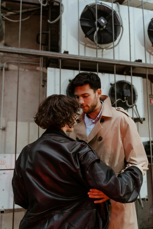 a man standing next to a woman in front of a building, in a brown leather maxi jacket, comforting, gay rights, alessio albi and shin jeongho