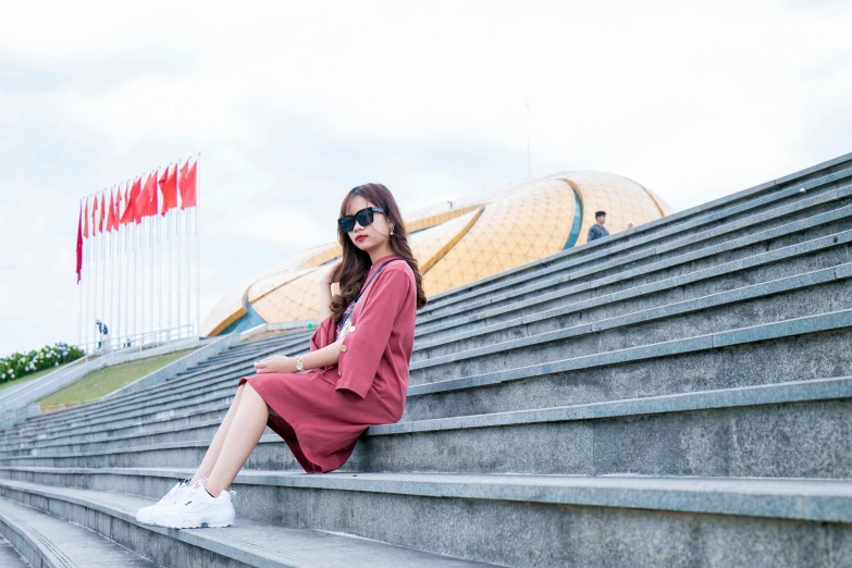 a woman sitting on the steps of a building, inspired by Cui Bai, pexels contest winner, maroon red, tiananmen square, modern casual clothing, on display