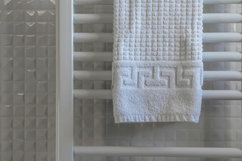 a towel hanging on a towel rack in a bathroom, an ambient occlusion render, inspired by Dod Procter, pexels contest winner, bauhaus, made of all white ceramic tiles, embossed, heated coils, checkered motiffs