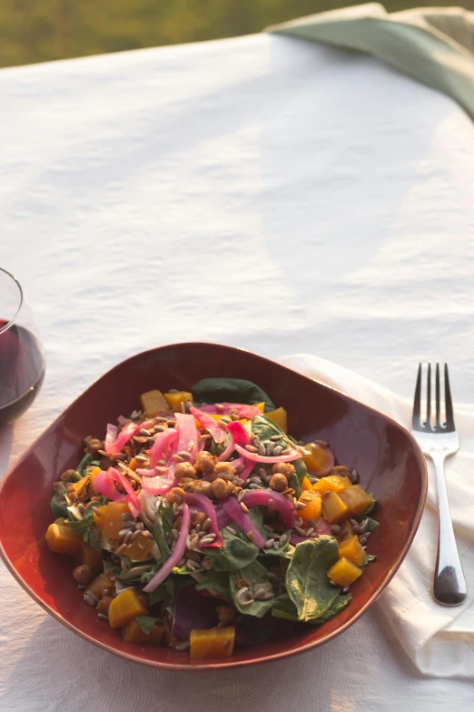 a plate of food and a glass of wine on a table, pink and teal and orange, seeds, prairie, salad