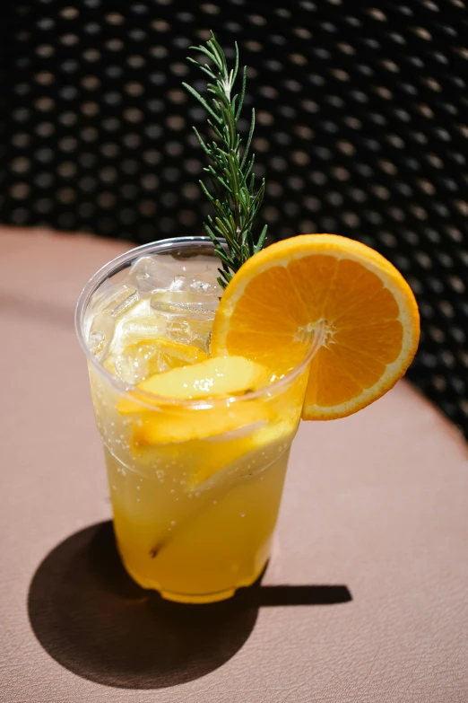 a glass of lemonade sitting on top of a table, orange slices, slush, sprigger, al fresco