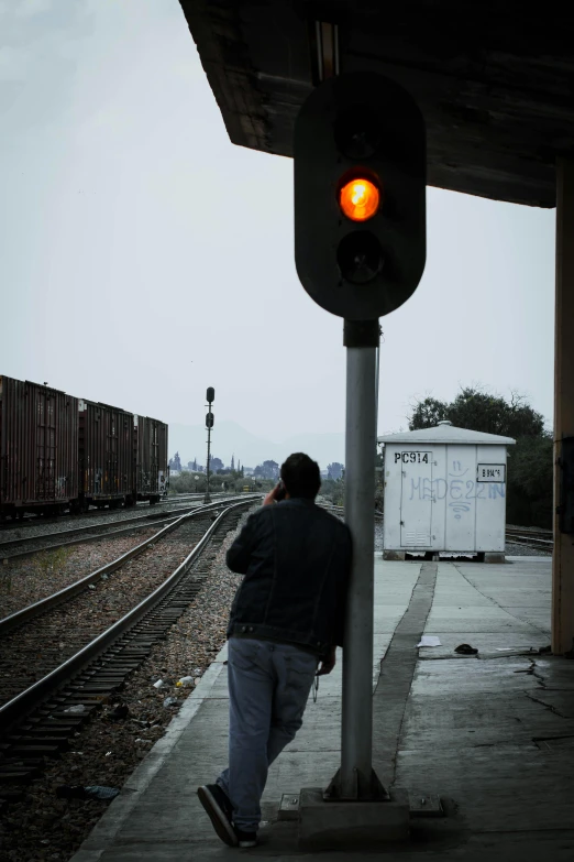 a man standing next to a traffic light at a train station, flickr, solitude seen in the distance, yard, port, low quality photo