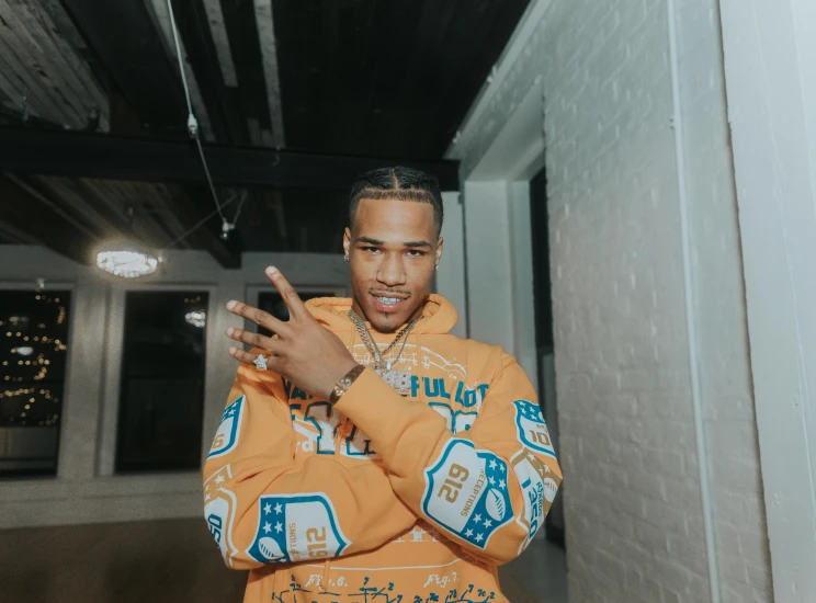 a man in an orange hoodie standing in a room, an album cover, trending on pexels, rapper jewelry, giving a thumbs up, profile image, cocky smirk