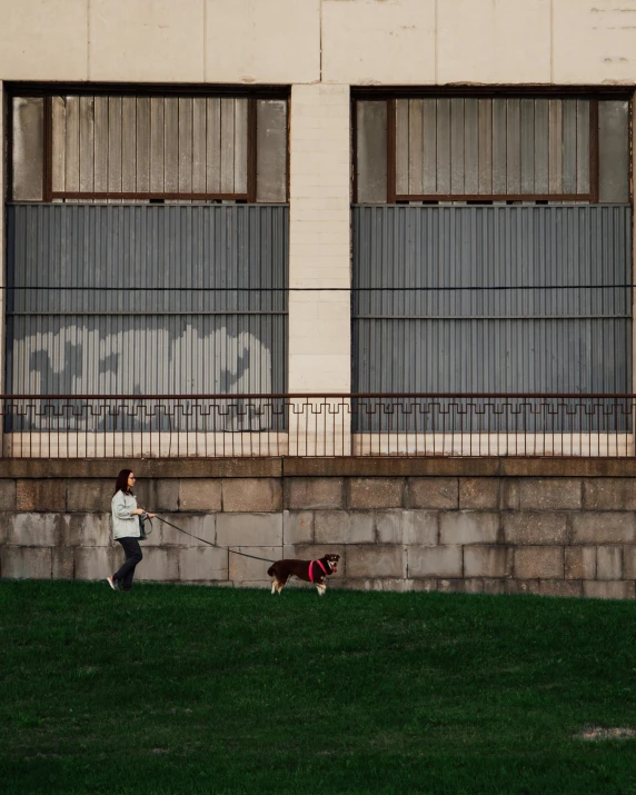 a woman walking a dog on a leash in front of a building, by Lucia Peka, pexels contest winner, city park, grazing, ignant, tense