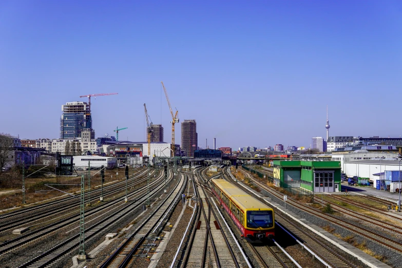 a train traveling down train tracks next to a city, palast der republik in berlin, fan favorite, construction, city skyline