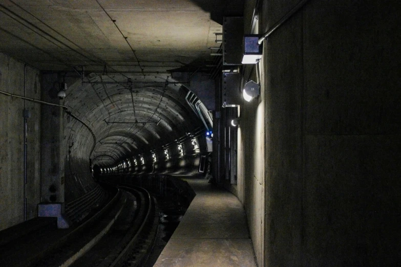 a train traveling through a tunnel next to a train track, a portrait, unsplash, conceptual art, underground bunker, musee d'orsay 8 k, search lights, opposite the lift-shaft