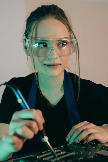 a woman in safety glasses working on a computer, by Adam Marczyński, smoking soldering iron, portrait n - 9, student, glow