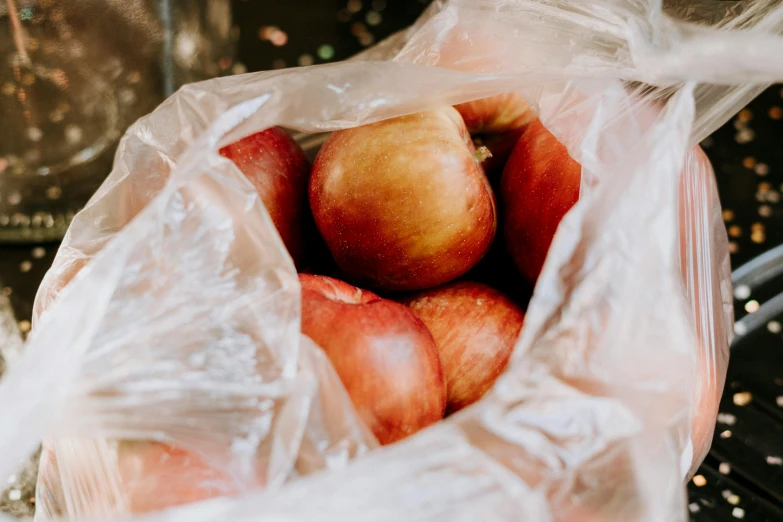 a plastic bag full of apples on the ground