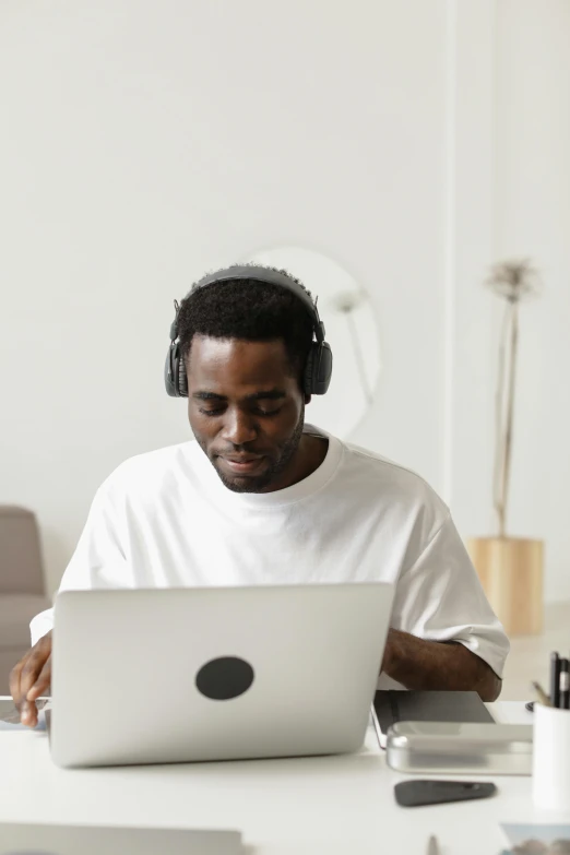 a man sitting at a table with a laptop and headphones, by Carey Morris, trending on pexels, afrofuturism, an all white human, at home, slightly minimal, performing