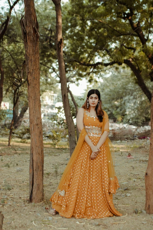 a woman standing in the middle of a forest, inspired by Saurabh Jethani, pexels contest winner, orange and yellow costume, in a city park, looking regal and classic, square