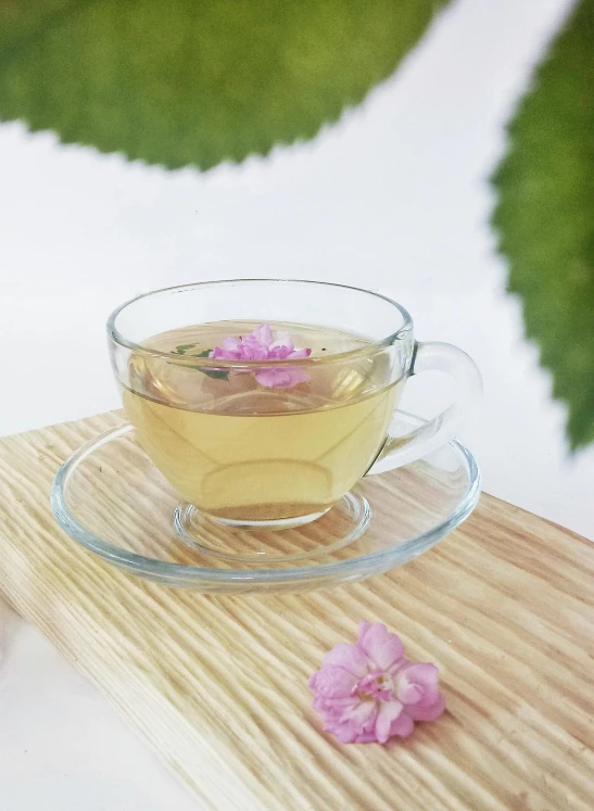 a cup of tea sitting on top of a wooden table, a digital rendering, inspired by Tan Ting-pho, pexels, moth orchids, green and pink, full body close-up shot, romantic greenery