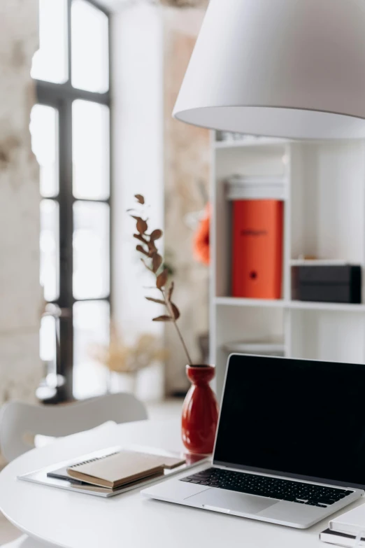 a laptop computer sitting on top of a white table, pexels contest winner, light and space, crimson accents, tall ceilings, orange lamp, clean and organized